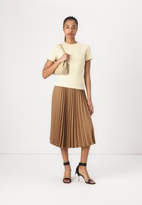 Light yellow fitted t-shirt, brown pleated midi skirt, black ankle-strap heels, and a tan handbag, against a plain white background.