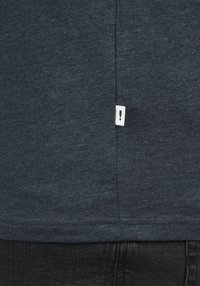 Navy blue cotton t-shirt with a soft texture, featuring a small white label with an exclamation mark on the left side seam.