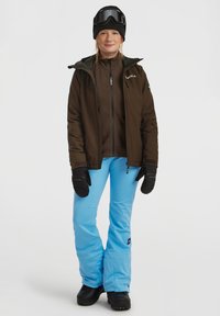 Skikleding met een bruine waterdichte jas, lichtblauwe broek, zwarte handschoenen en een zwarte beanie met goggles. Geschikt voor wintersport.