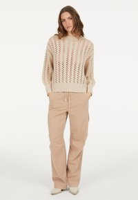 Hellbeige gestrickter Pullover mit lockerer Passform, der offene Strickmuster und gerippte Bündchen aufweist, kombiniert mit bequemen, hellbeigen Hosen.