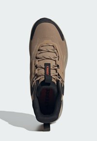 Svetlohnedá a čierna športová obuv s horným dielom z sieťoviny, textúrovaným povrchom, systémom šnurovania, pútkom a logom "TERREX" na jazyku.