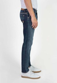 Slim-fit donkerblauwe denim jeans met contrasterende stiksels en een rits. Draagt men ze met witte sneakers, dan ontstaat er een casual uitstraling.