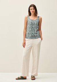 Grön och vit mönstrad urringad topp med geometrisk design, ihop med ljusbeige vida byxor och mörkgröna sandaler.