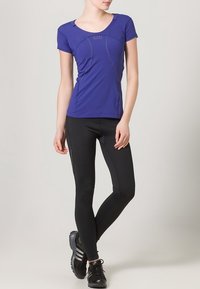 Maglietta sportiva corta viola con cuciture curve, abbinata a leggings neri aderenti. Il modello indossa scarpe da ginnastica nere. Design semplice, tessuto leggero.