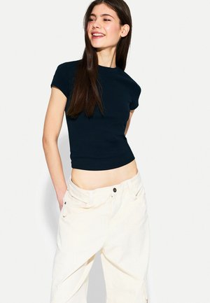 Marineblauwe korte mouwen cropped t-shirt van soepele stof, gecombineerd met lichtbeige wijde broek met zijzakken en knoopsluiting.