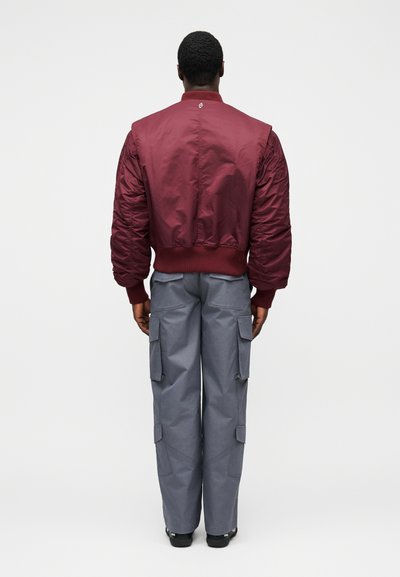 Vínovo červená prešívaná bunda s rebrovanými manžetami a golierom, kombinovaná so sivými cargo nohavicami s bočnými vreckami a voľným strihom.