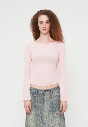 Top rosa a maniche lunghe con scollo smerlato e design testurizzato, abbinato a una gonna grigia con motivo a pelle di serpente.