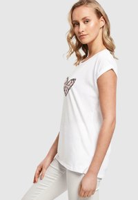 Hvid bomuld t-shirt med rullede korte ærmer, der har et pink og sort leopardprint hjerte-design på forsiden. Enkel og afslappet stil.