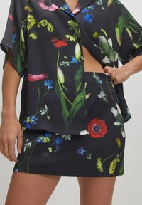 Bloemmotiefoutfit met een zwarte achtergrond. De top heeft een losse pasvorm met korte mouwen en een knoopsluiting. De bijpassende rok sluit goed aan.