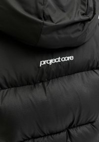 Melnā pūkā jaka ar teksturētu apdari un kapuci. Aizmugurē ar baltu izšūtu "project care" logo.