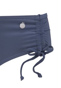 Marineblauwe bikini onderstuk met rimpelingen aan de zijkanten, verstelbare strik en een klein metallic logo detail nabij de taille. Glad textuur.