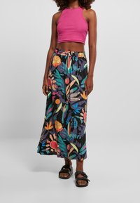 Blommig maxikjol i svart, med livfulla färgglada blommor och löv, ihop med en rosa kort topp och svarta sandaler.