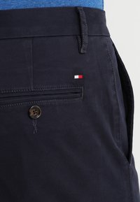 Marina blå byxor i texturerad tyg, med en sidoficka som har knappstängning och en liten tri-färgad flaggaemblem.