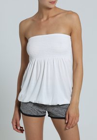 Weißes trägerloses Oberteil mit gerafftem Oberteil und fließender Passform, kombiniert mit schwarzen und grauen Sportshorts mit kontrastierendem Bund.
