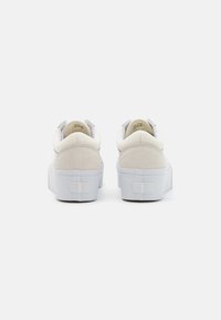 Bílé slip-on tenisky se svrchním materiálem z usně a kůže, zvýšenou bílou gumovou podrážkou a minimálním brandováním na zadní straně. Hladká textura s zaobleným podpatkem.