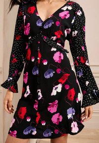 Črna obleka z cvetličnim vzorcem v rdeči, roza in vijolični barvi. Ima dolge rokave s pikami in ovit dizajn, ter gumbe spredaj.