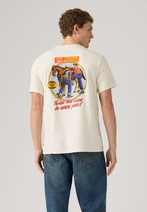 Mees, kes kannab valget Levi Strause T-särki, millel on värvikas vintage-logo kahe kova ja hobusega, tekstiga "Kahekordne vastupidavus igas paaris!"