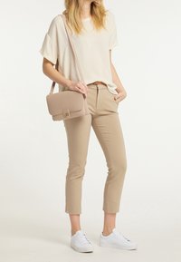 Beige crossover taske med en guldfarvet spænde, båret med en løs cremefarvet bluse og tætsiddende beige bukser, parret med hvide sneakers.