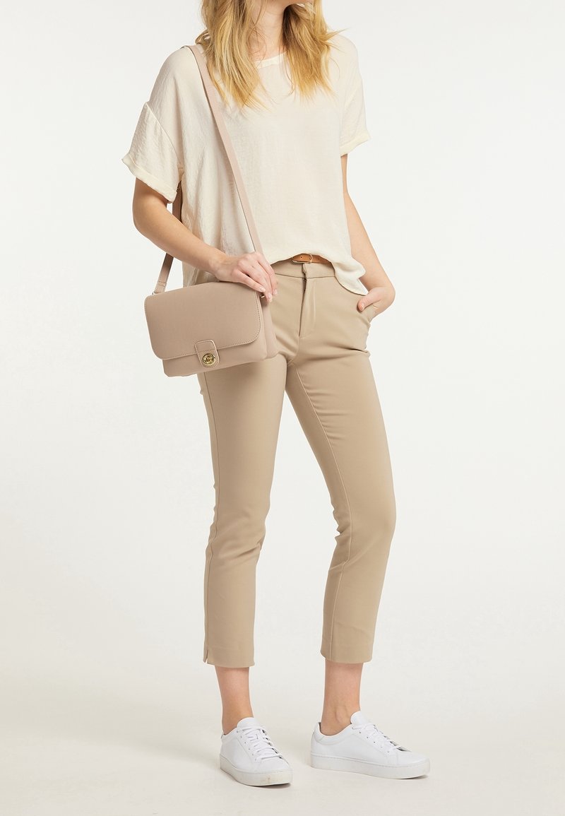 Beige crossover taske med en guldfarvet spænde, båret med en løs cremefarvet bluse og tætsiddende beige bukser, parret med hvide sneakers.