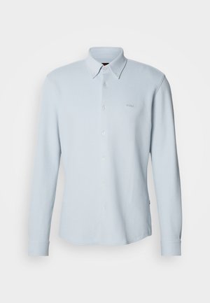 Gaiši zils, garām piedurknēm ar pogām aiztaisāms krekls. Izgatavots no strukturēta auduma ar klasisku apkakli, uz krūškurvja atrodas neliels logotips, un piedurkņu galiem ir pogas.