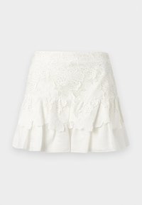 Minifalda blanca de encaje con bordado floral y dobladillo con volantes, superpuesta sobre un fondo de tela blanca sólida.