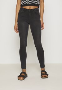 Jeans skinny negros, tela de mezclilla, diseño de cintura alta, costuras mínimas, combinados con sandalias negras de tiras con hebilla y suela de corcho.