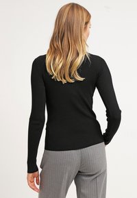 Svart ribbad långärmad topp med figurnära passform, rund halsringning och texturerat tyg. Kombinerad med gråa byxor med smala ränder.