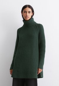 Mørkegrøn strikket sweater med høj krave, ribbet tekstur, lange ærmer og slidser i siden for nem bevægelse.