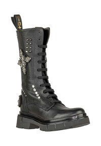 Stivale in pelle nera con lacci e suola spessa, dettagli borchiati e decorazioni a forma di farfalla di cristallo sul lato.