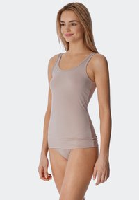 Débardeur beige clair avec des bretelles fines, de coupe ajustée et une texture côtelée subtile. Associé à une culotte taille haute assortie.