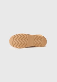 Semelle de chaussure présentant un motif texturé avec des rainures en zigzag, fabriquée en caoutchouc marron clair, design plat et bords lisses.