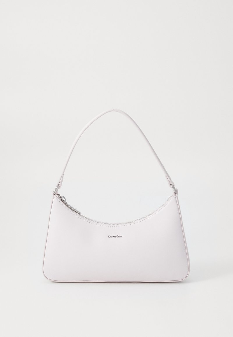 Sac à épaule blanc Calvin Klein avec fermeture éclair supérieure incurvée et courte bandoulière réglable sur fond uni.
