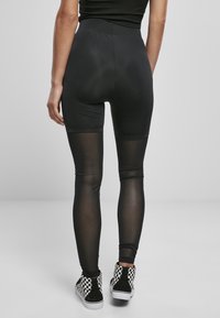 Svarta leggings med hög midja, med en genomskinlig panel på de nedre benen. Outfitten matchas med rutiga hög-top sneakers.