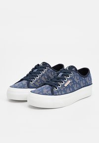 Scarpe da ginnastica in tela blu scuro con un design a motivo. Presentano suola in gomma bianca, lacci in tinta e una targhetta con il marchio sul lato.