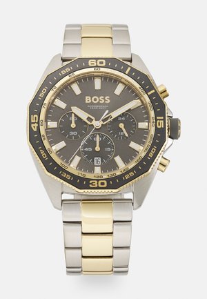 Chronograph-Uhr mit einer schwarzen und goldenen Lünette, grauem Zifferblatt, drei Sub-Dials und einem Armband aus Edelstahl mit goldenen Akzenten.