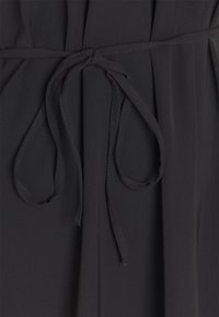 Schwarzes Stoffkleidungsstück mit einer gebundenen Taille und langen, dünnen Trägern. Das Material ist glatt mit einem leichten Glanz und subtilen Drapierungsdetails.
