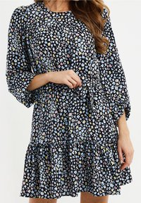 Vestido negro de manga larga con dobladillo con volantes, que presenta un patrón floral multicolor en azul, rosa y amarillo. Tejido ligero y corte relajado.
