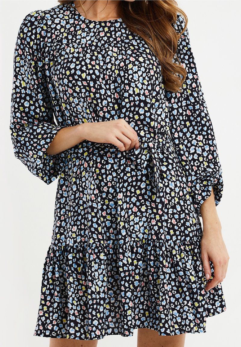 Vestido negro de manga larga con dobladillo con volantes, que presenta un patrón floral multicolor en azul, rosa y amarillo. Tejido ligero y corte relajado.