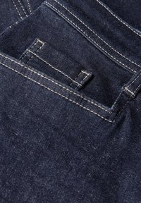 Mörkblå denimtyg med en närbild av en bakficka. Vita sömmar omger fickan och sömmarna, med en något texturerad yta.