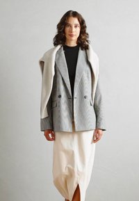 Striped blazer in gray and white over a black top, paired with a cream midi skirt featuring a front slit. Smooth texture, structured fit.