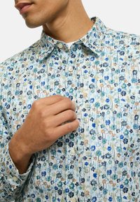 Hemd mit Knopfleiste und Blumenmuster in Hellblau mit grünen, marineblauen und beigen Akzenten. Hergestellt aus leichtem Stoff mit strukturierter Optik.