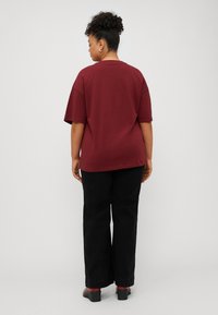 Burgundy oversized T-shirt with short sleeves, rounded neckline, and smooth fabric, paired with black wide-leg pants and block-heeled shoes.