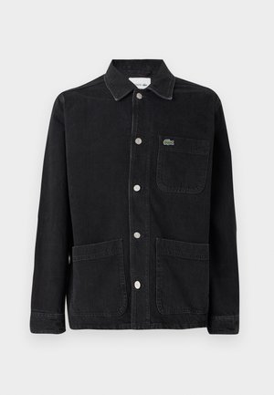 Giacca in denim nera con colletto, bottoni argentati, due tasche frontali e un piccolo logo verde Lacoste sulla tasca del petto.