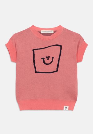 Roza pletena pulover s kratkimi rokavi, na sprednji strani z črnim okvirjem v obliki kvadrata in nasmejanim obrazom ter majhno belo znamko na robu.