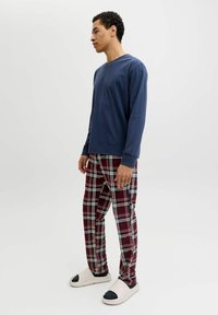 Chemise à manches longues navy, pantalon à carreaux rouges et blancs, et chaussures à enfiler blanches avec des accents navy. Tissu lisse avec une coupe décontractée.