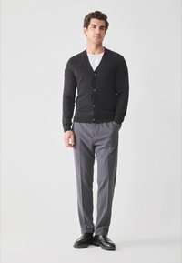 Black cardigan with five buttons, worn over a white T-shirt, paired with gray slacks and black dress shoes. Minimalist design, lightweight fabric.