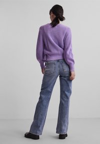 Fioletowy sweter dzianinowy o żebrowanej fakturze z tylnym zapięciem, połączony z jasnoniebieskimi spodniami typu wide-leg i czarnymi butami.