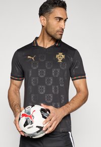 Melnas futbola kreklas ar smalku vairogu rakstu, zelta Puma logo un Portugāles emblēmu. Apkaklē kontrastējošas zaļas un sarkanas detaļas.