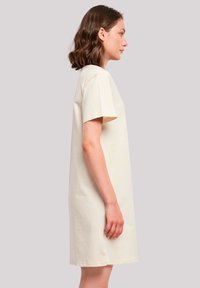Crème-kleurige katoenen t-shirt jurk, korte mouwen, ontspannen pasvorm, knielengte, gladde textuur, eenvoudig ontwerp zonder zichtbare patronen of accenten.