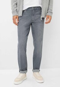 Jeans in denim grigio con taglio dritto, dotati di chiusura con zip e bottone, orli arrotolati e indossati con sneakers color crema.